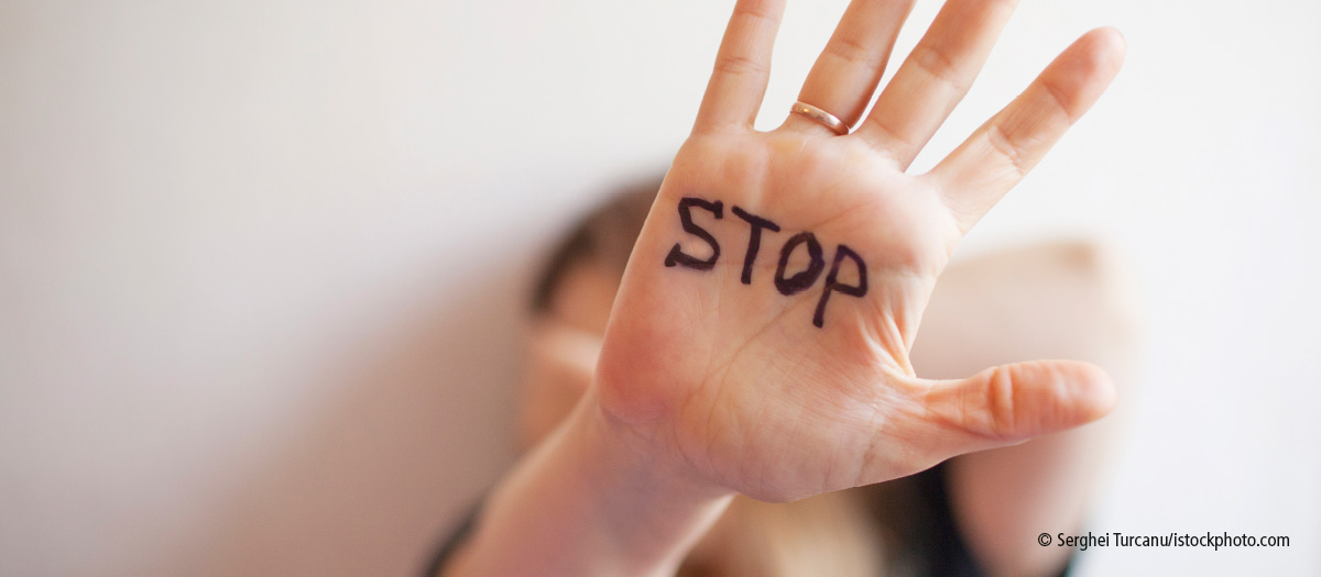 Eine Hand mit Ring und der Aufschrift "STOP" wird schützend vor das Gesicht gehalten.